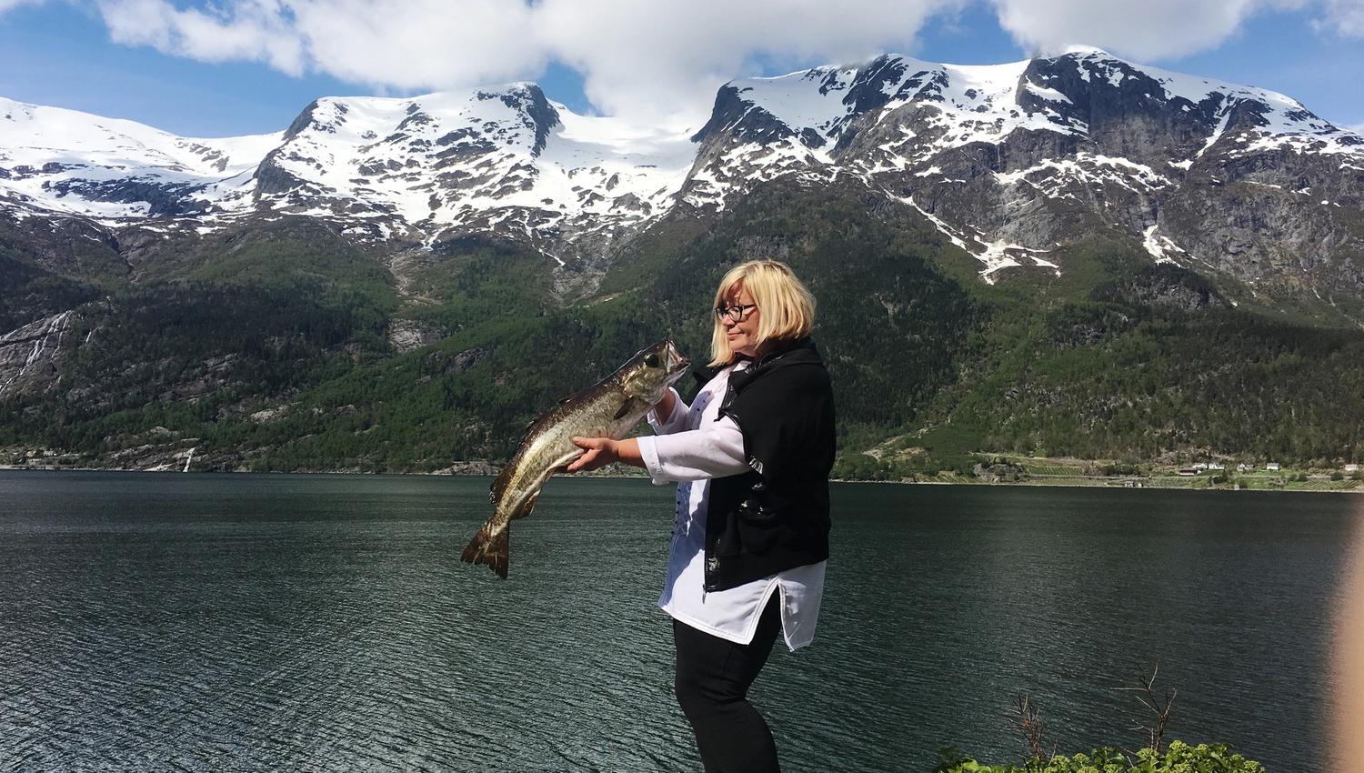 Happy guest proudly holding a large fish by the fjord at Stana Gard – a true fishing experience in the Hardanger region.
