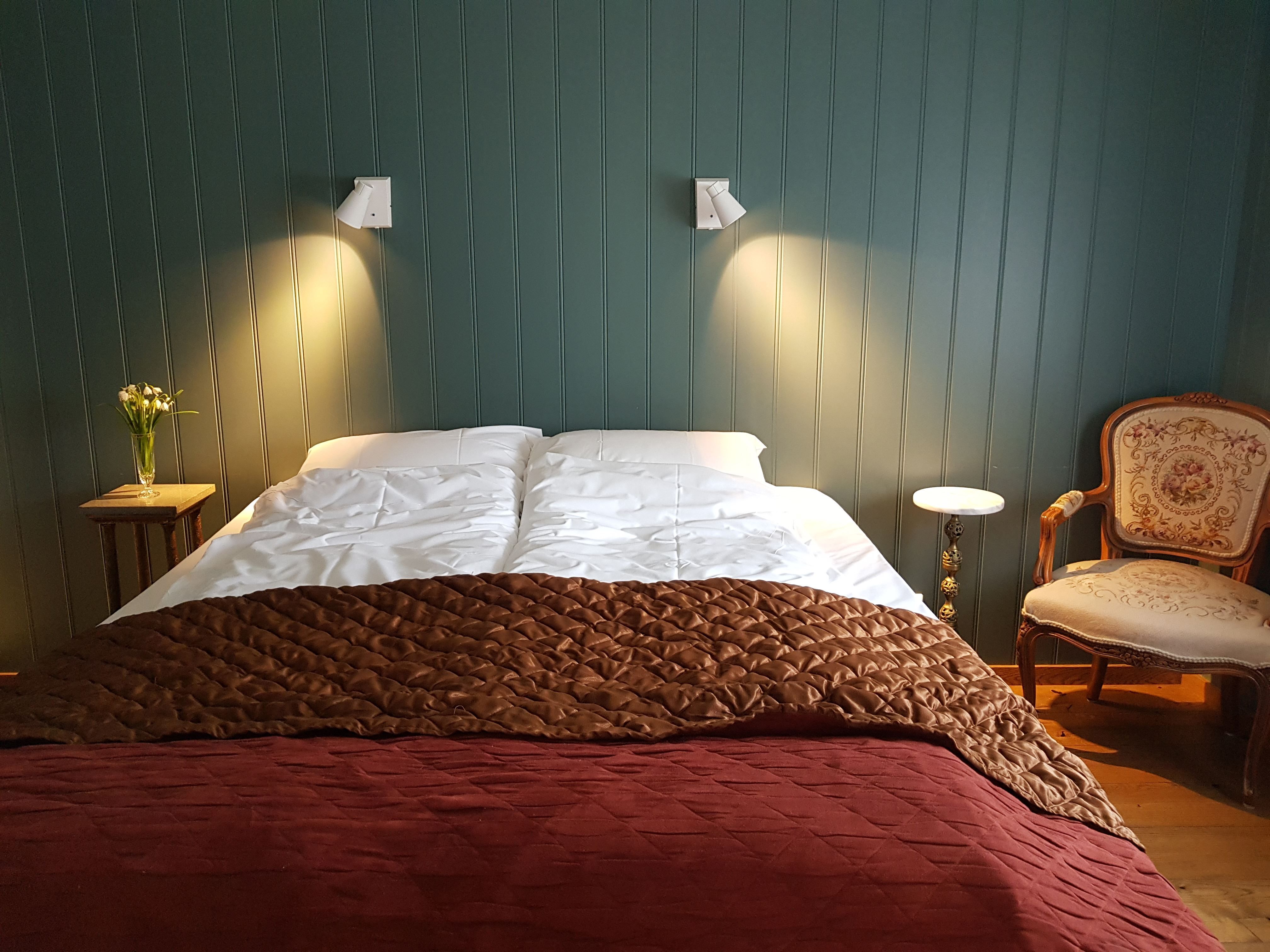 Orheimstunet in Nordfjord - Double bed with white pillows and layered brown and burgundy quilts, flanked by lit wall lamps and side tables..