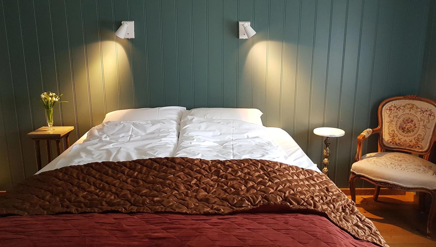 Orheimstunet in Nordfjord - Double bed with white pillows and layered brown and burgundy quilts, flanked by lit wall lamps and side tables..