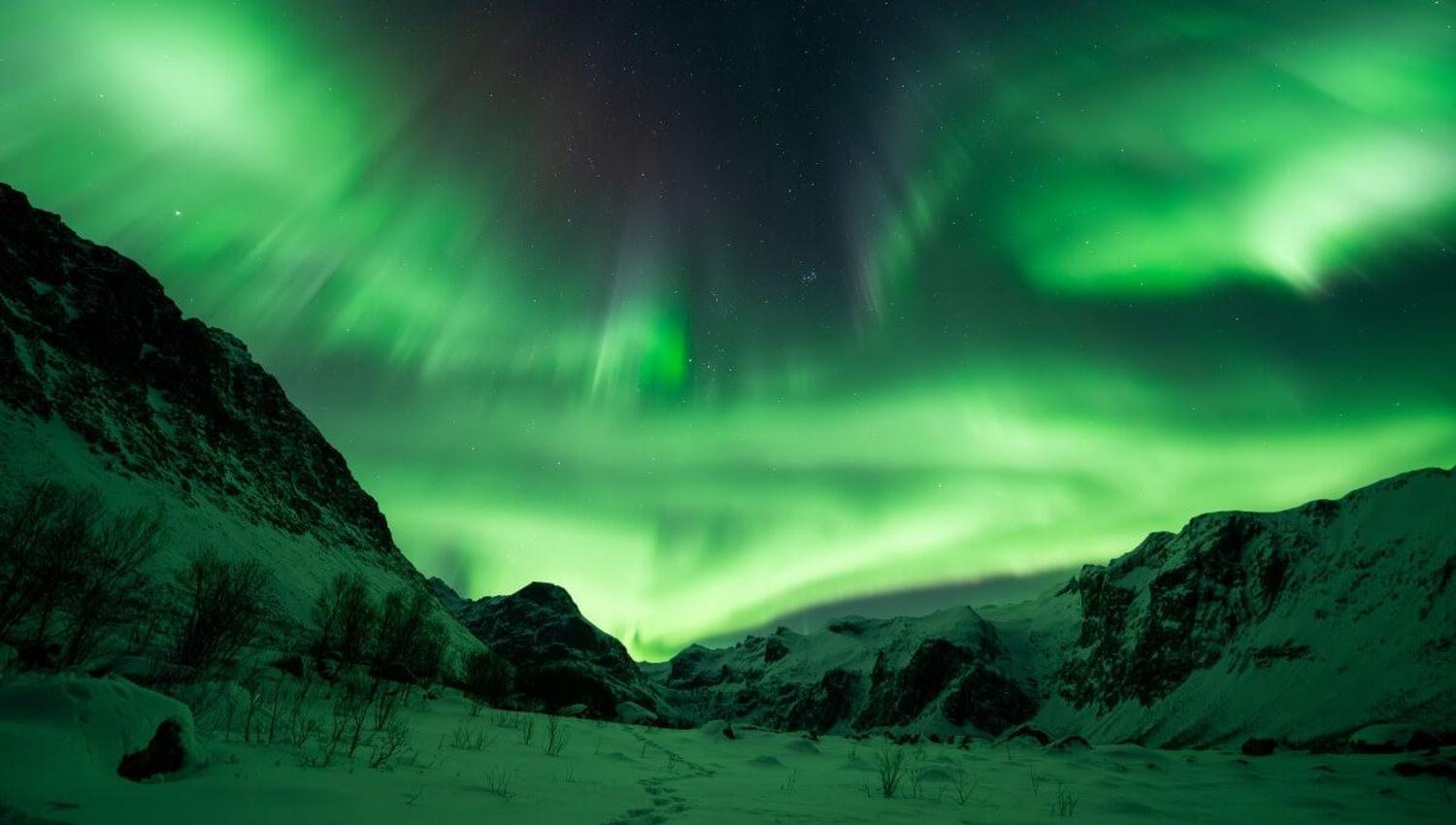 The Northern Lights appear from behind a mountain