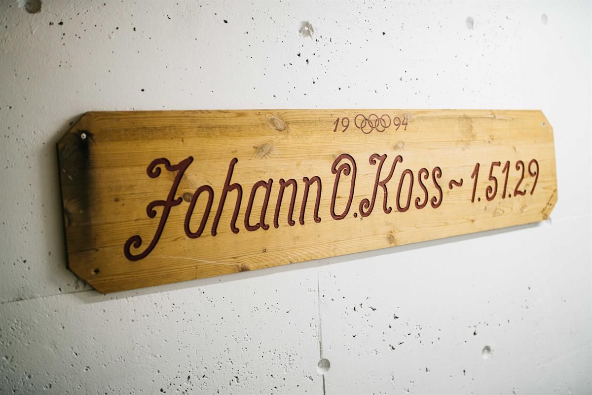 Wooden plaque mounted on a white wall, featuring engraved text and numbers.