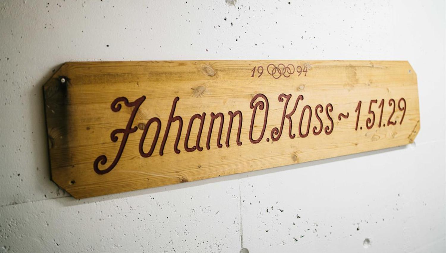 Wooden plaque mounted on a white wall, featuring engraved text and numbers.