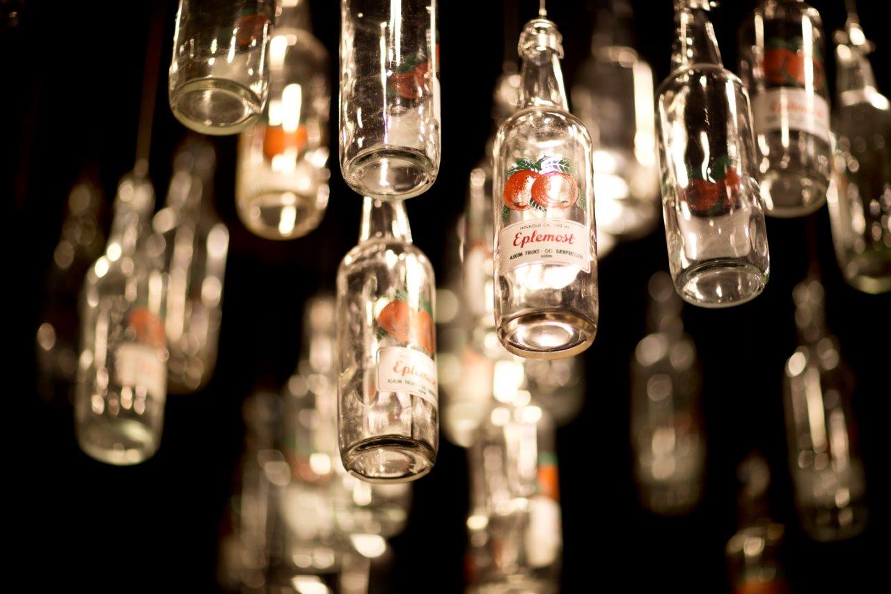Many glass bottles hang from the ceiling as decoration. The labels show red apples and the word “Apple Juice.”