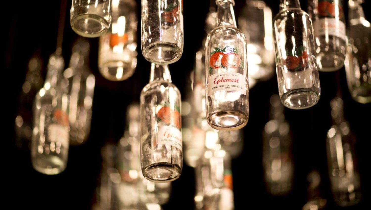 Many glass bottles hang from the ceiling as decoration. The labels show red apples and the word “Apple Juice.”