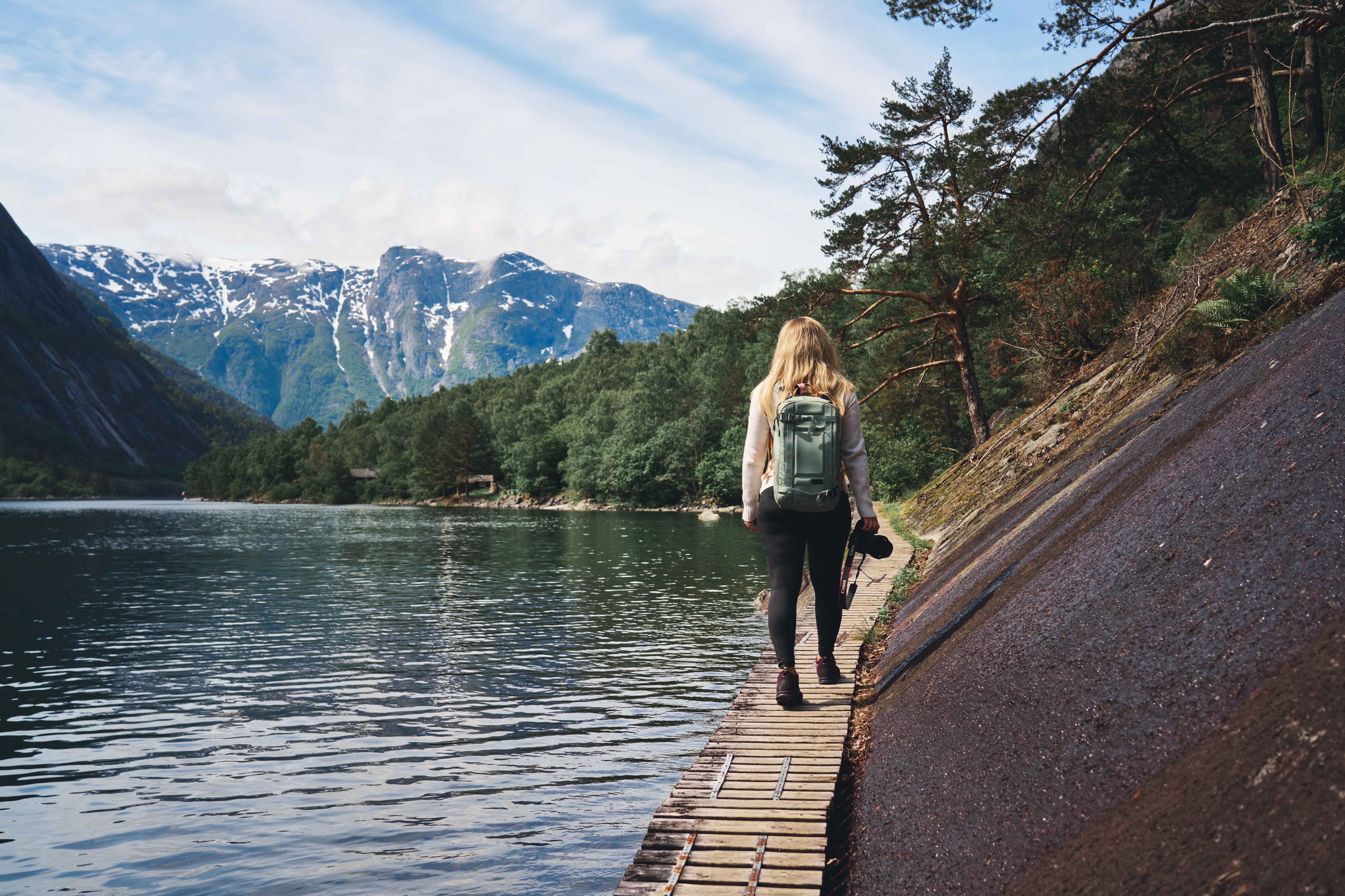 A female hiker walking on the wooden path boltet into the mountain wall next to the fjord.