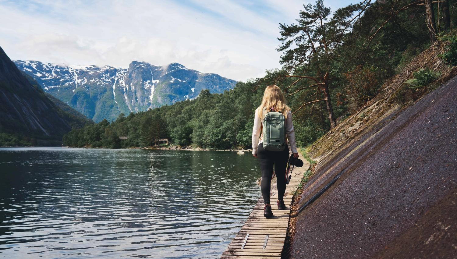 A female hiker walking on the wooden path boltet into the mountain wall next to the fjord.