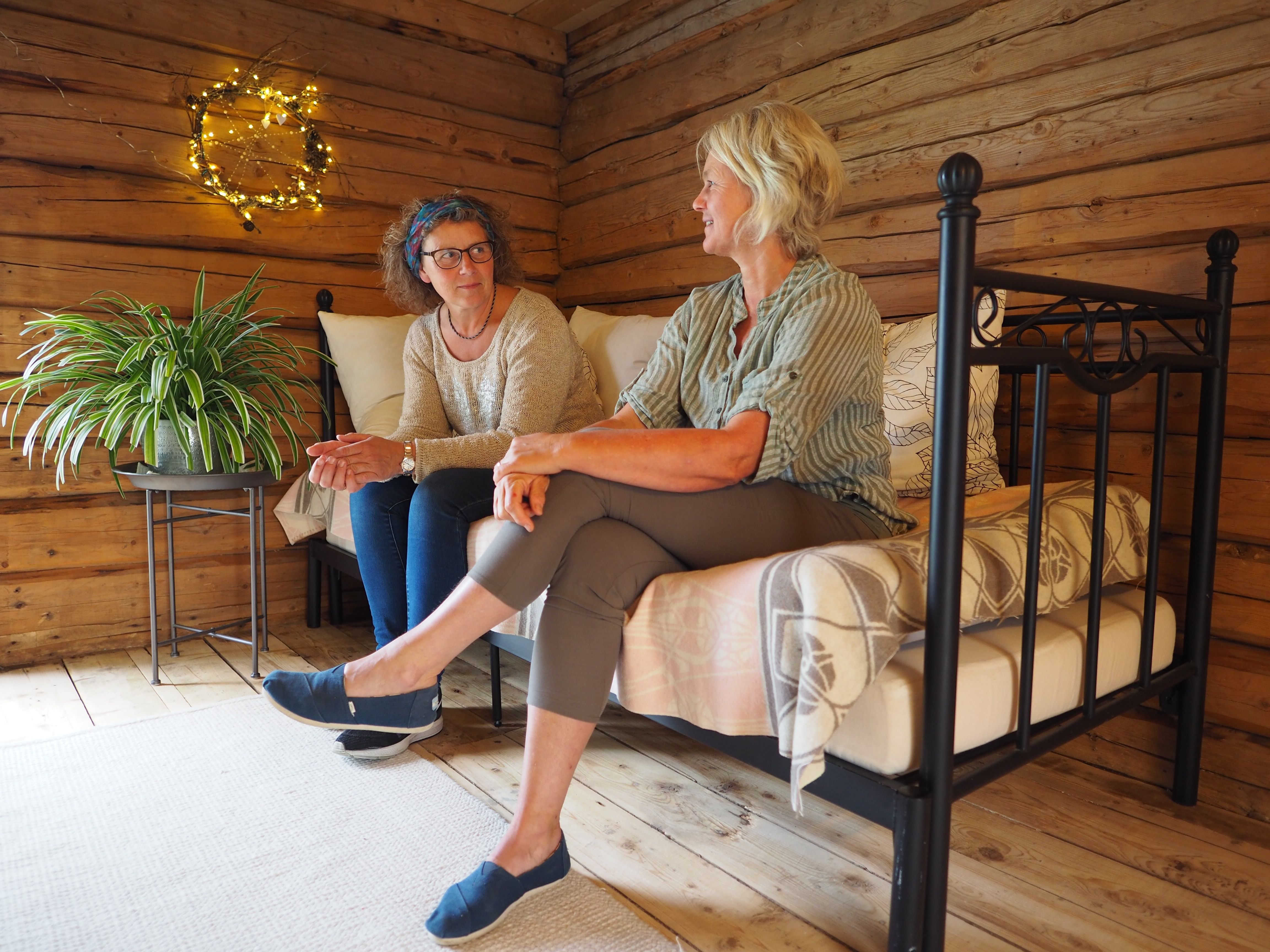 To damer prater mens de sitter i svar seng i stabburet, ved Lensmannsgården på Namdalseid