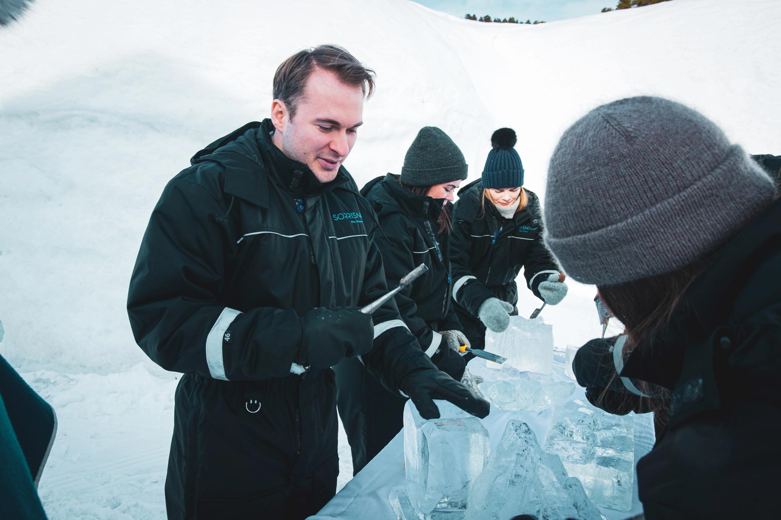 Groupe de personnes sculptant des blocs de glace dans un environnement neigeux.