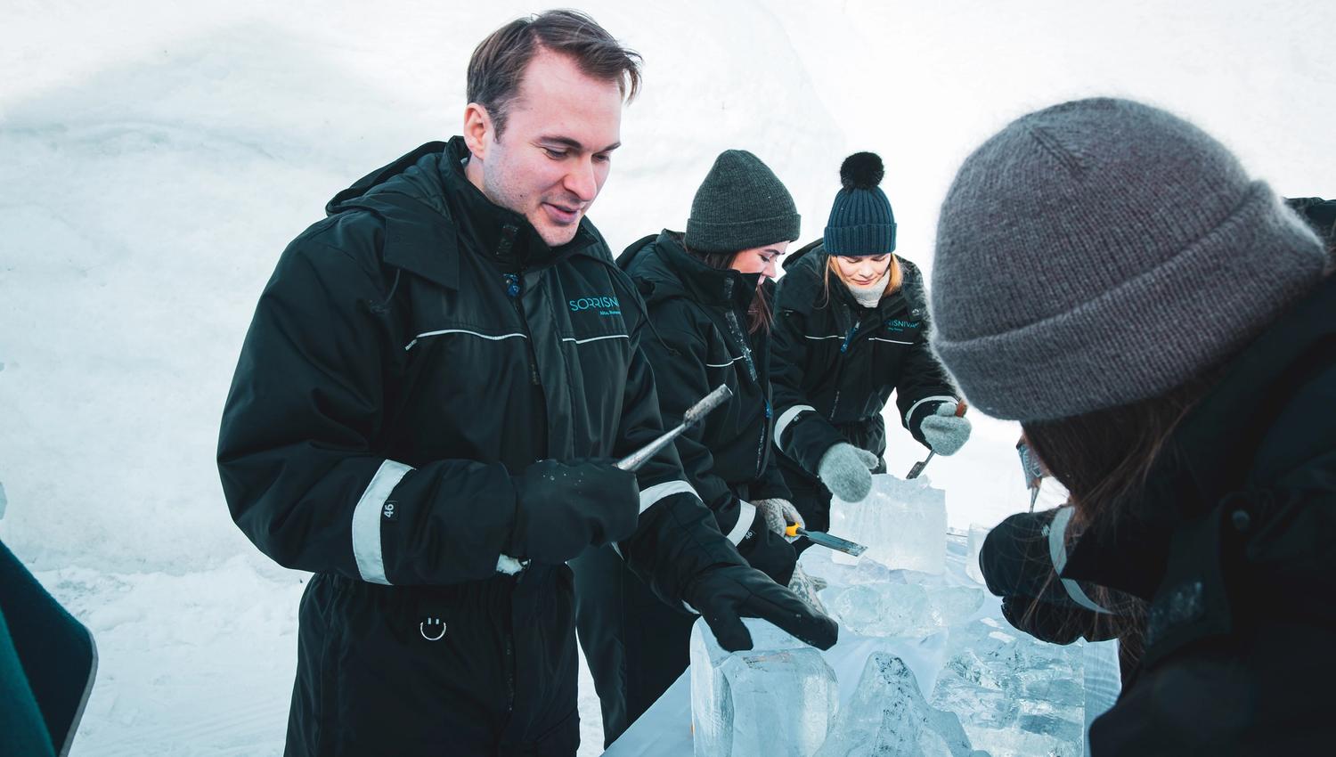Groupe de personnes sculptant des blocs de glace dans un environnement neigeux.