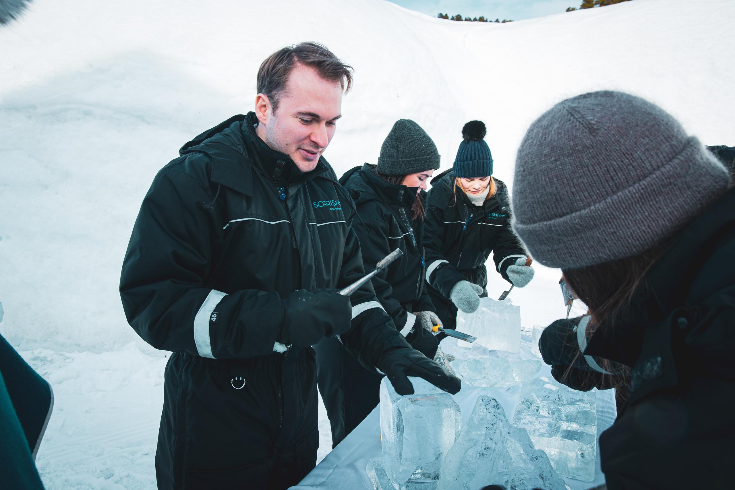 Groupe de personnes sculptant des blocs de glace dans un environnement neigeux.