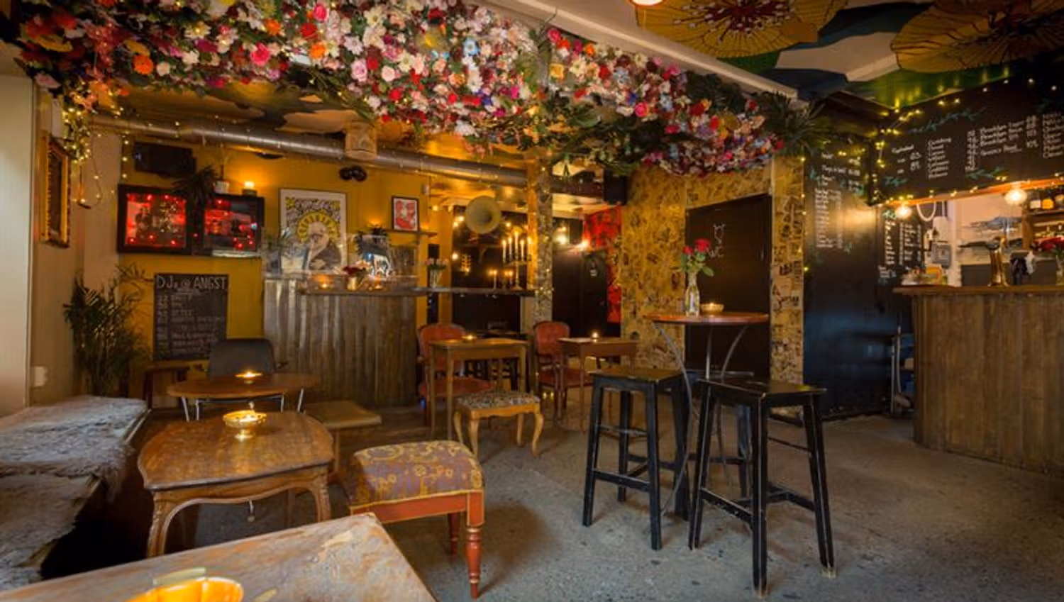 Interior of bar area with various tables and chairs in different sizes. Flower arrangements hanging from the ceiling.