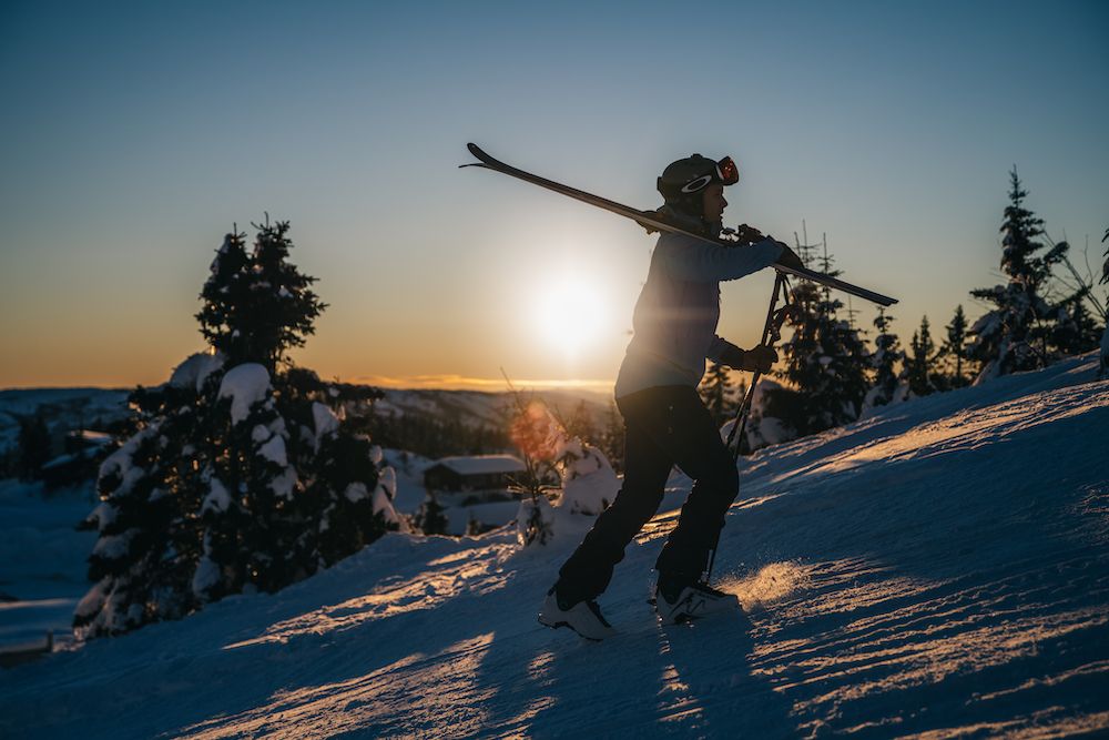 man walks up a hill with skis on his shoulder at Lifjell ski center in Bø 