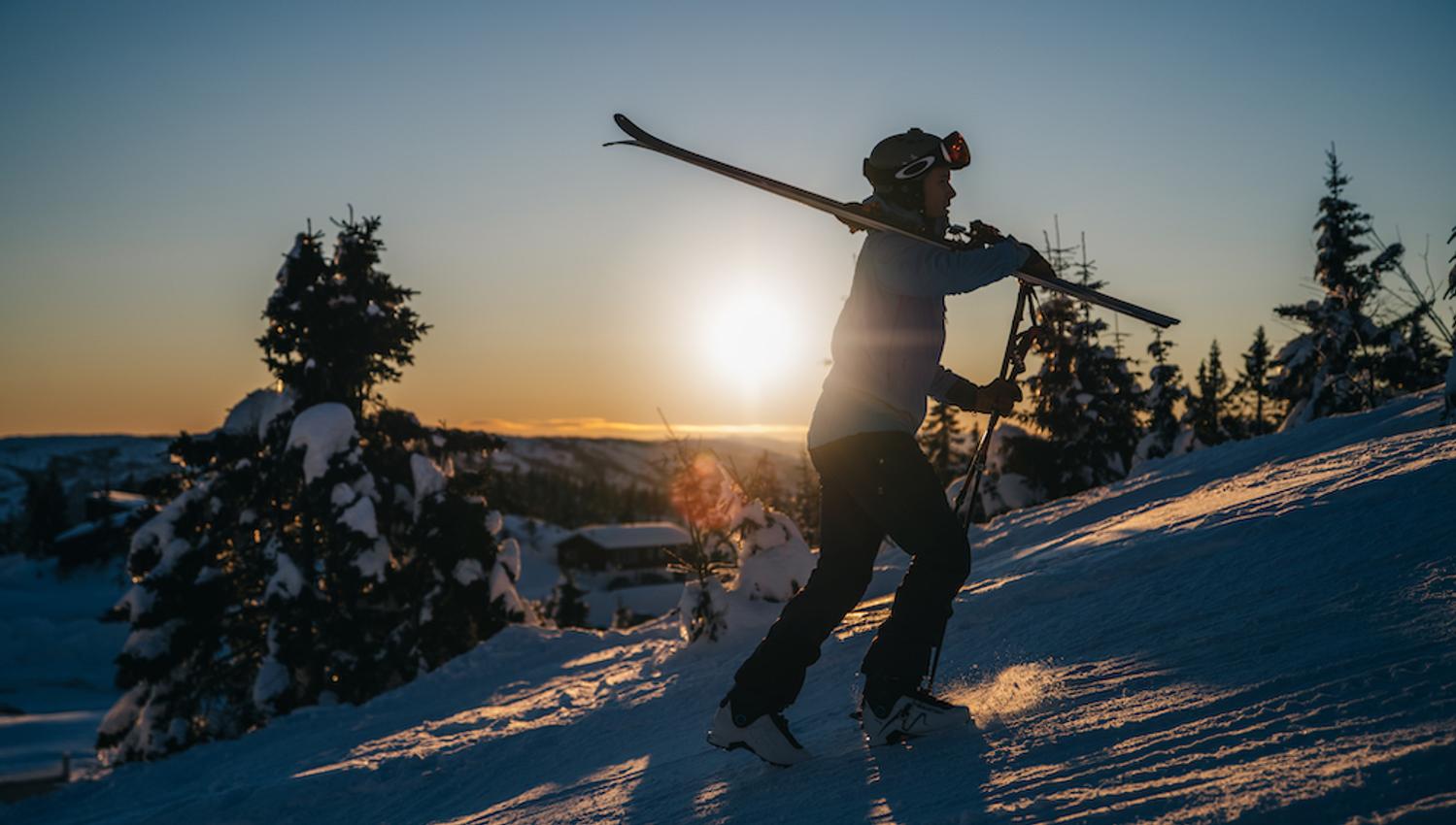 man walks up a hill with skis on his shoulder at Lifjell ski center in Bø