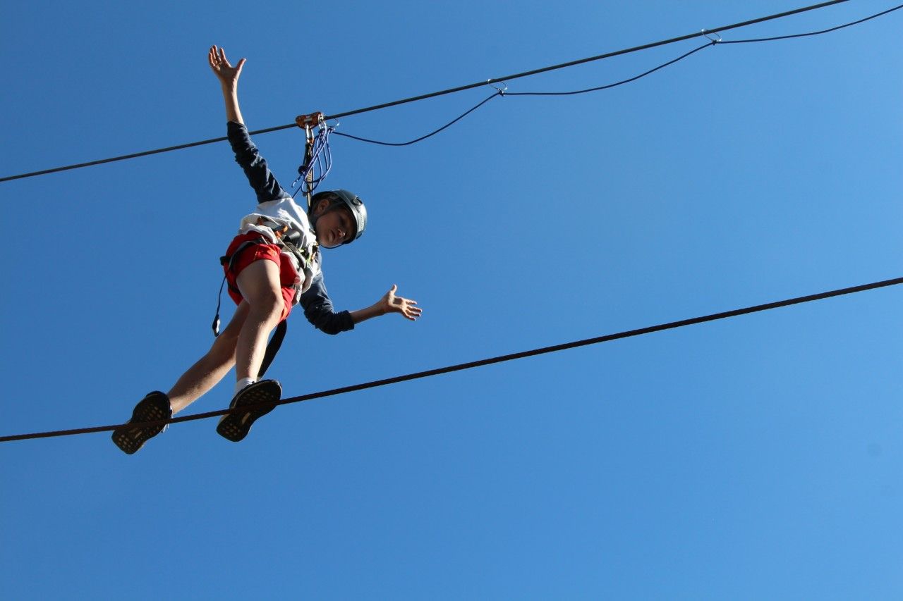 A boy balances on the climbing trail. The picture was taken from below, up against a clear blue sky.