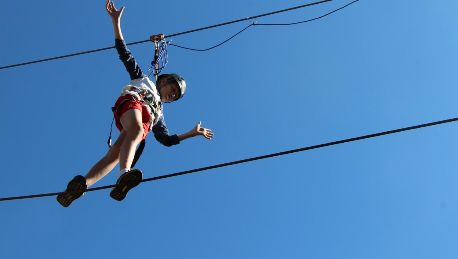 A boy balances on the climbing trail. The picture was taken from below, up against a clear blue sky.