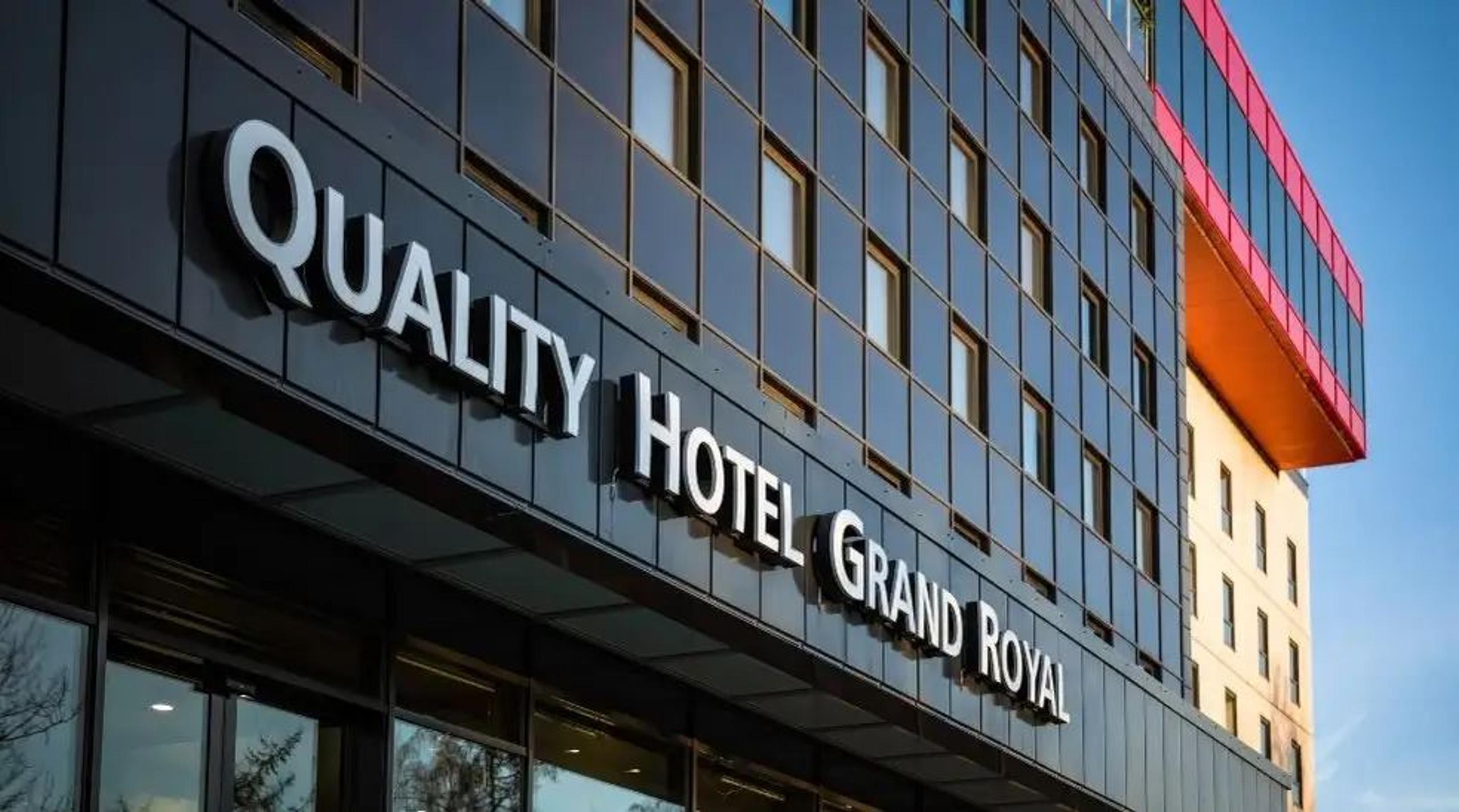 Angled view of a modern hotel facade with large letters reading “Quality Hotel Grand Royal” and many windows.