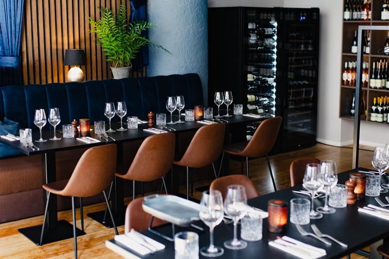 Blue seating section along the wall, black tables, brown chairs, wine cabinet in the corner