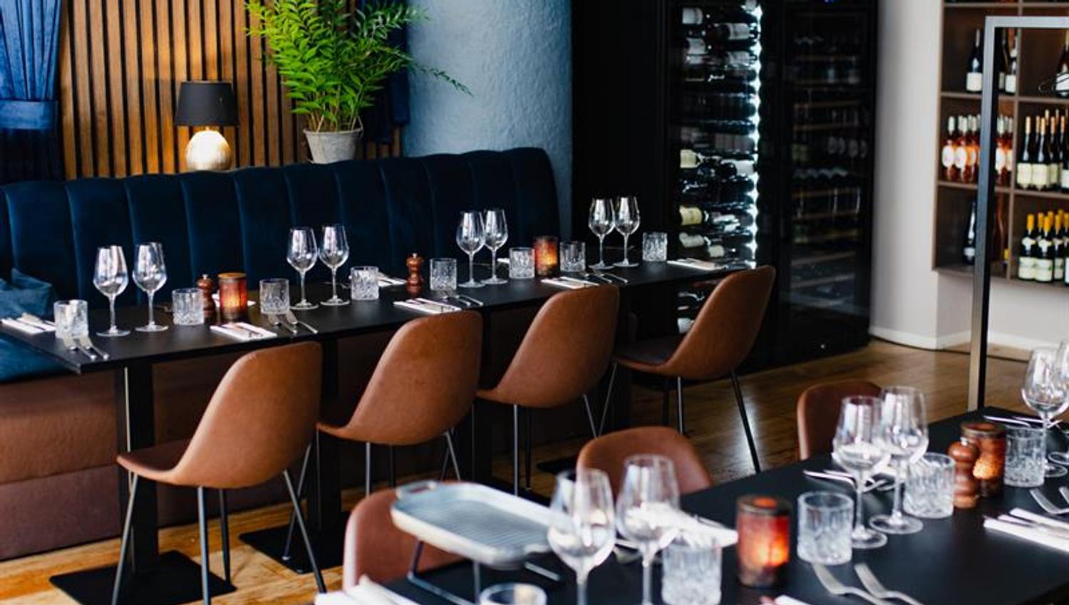 Blue seating section along the wall, black tables, brown chairs, wine cabinet in the corner