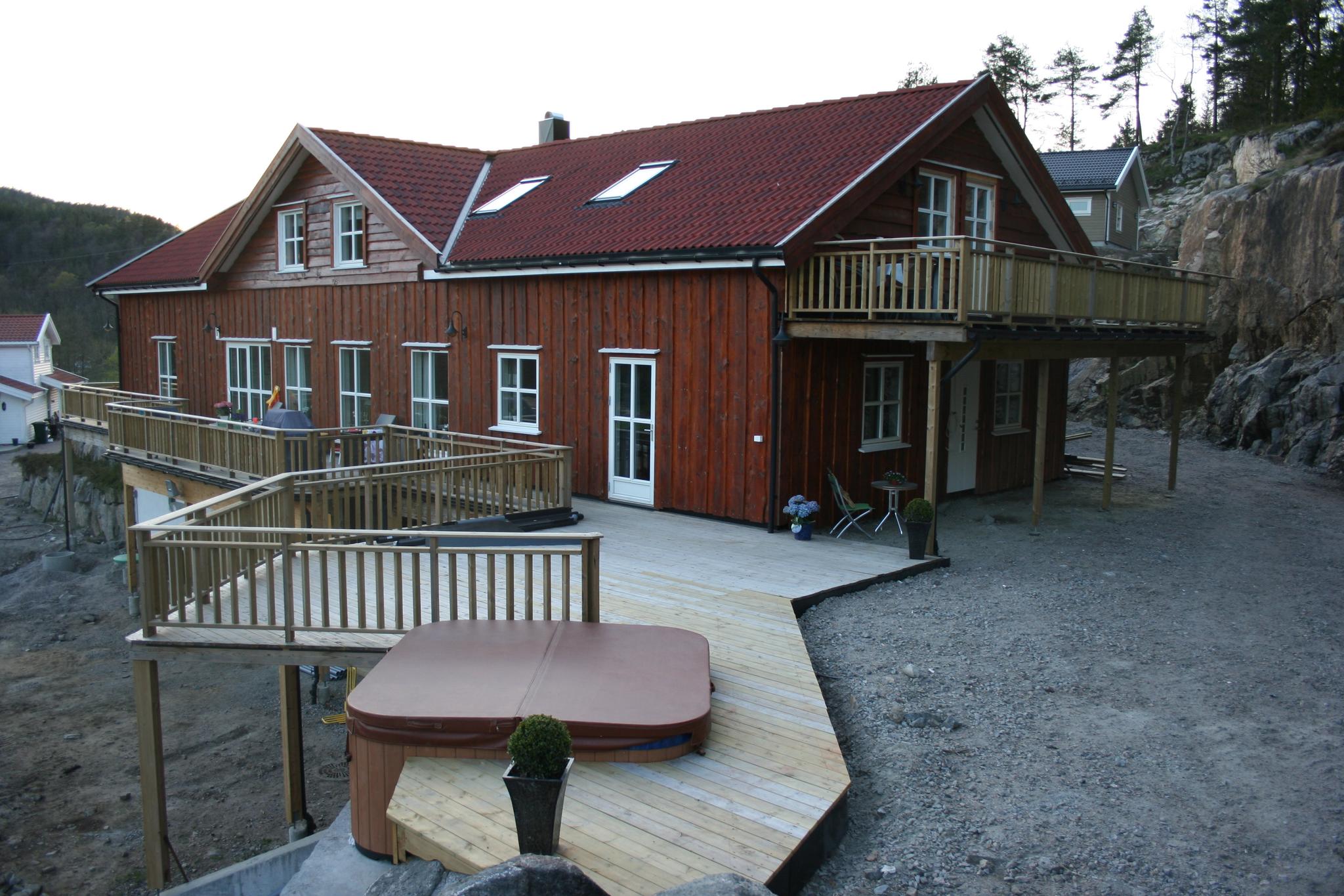 Brun hytte med balkong og terasse. Jacuzzi boblebad på terrassen.