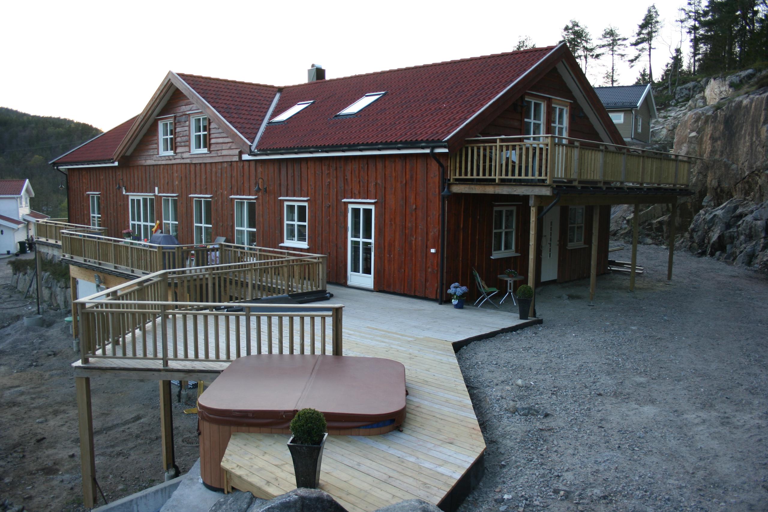 Brun hytte med balkong og terasse. Jacuzzi boblebad på terrassen.