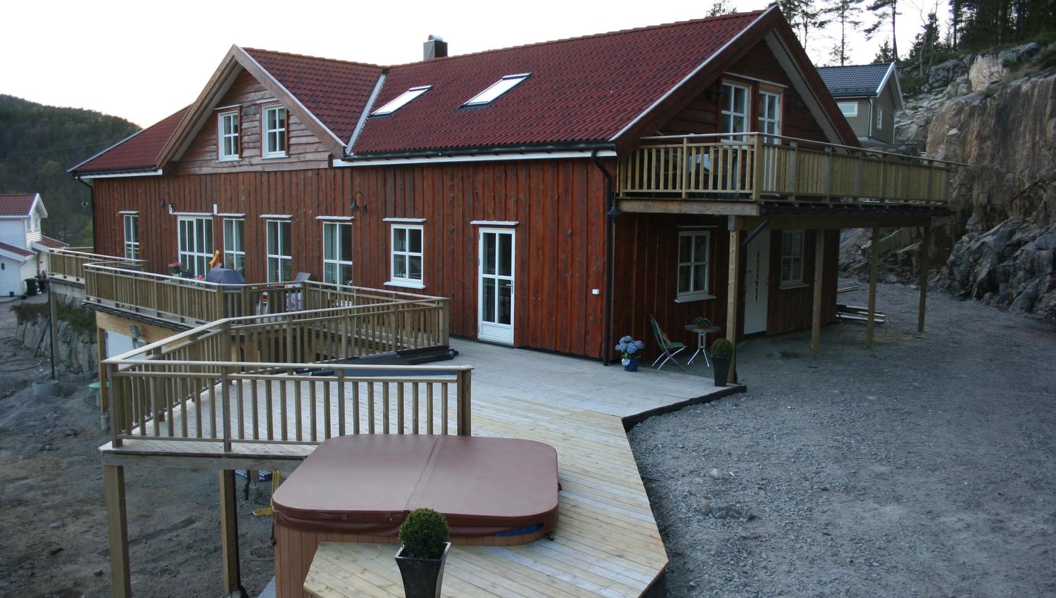 Brun hytte med balkong og terasse. Jacuzzi boblebad på terrassen.