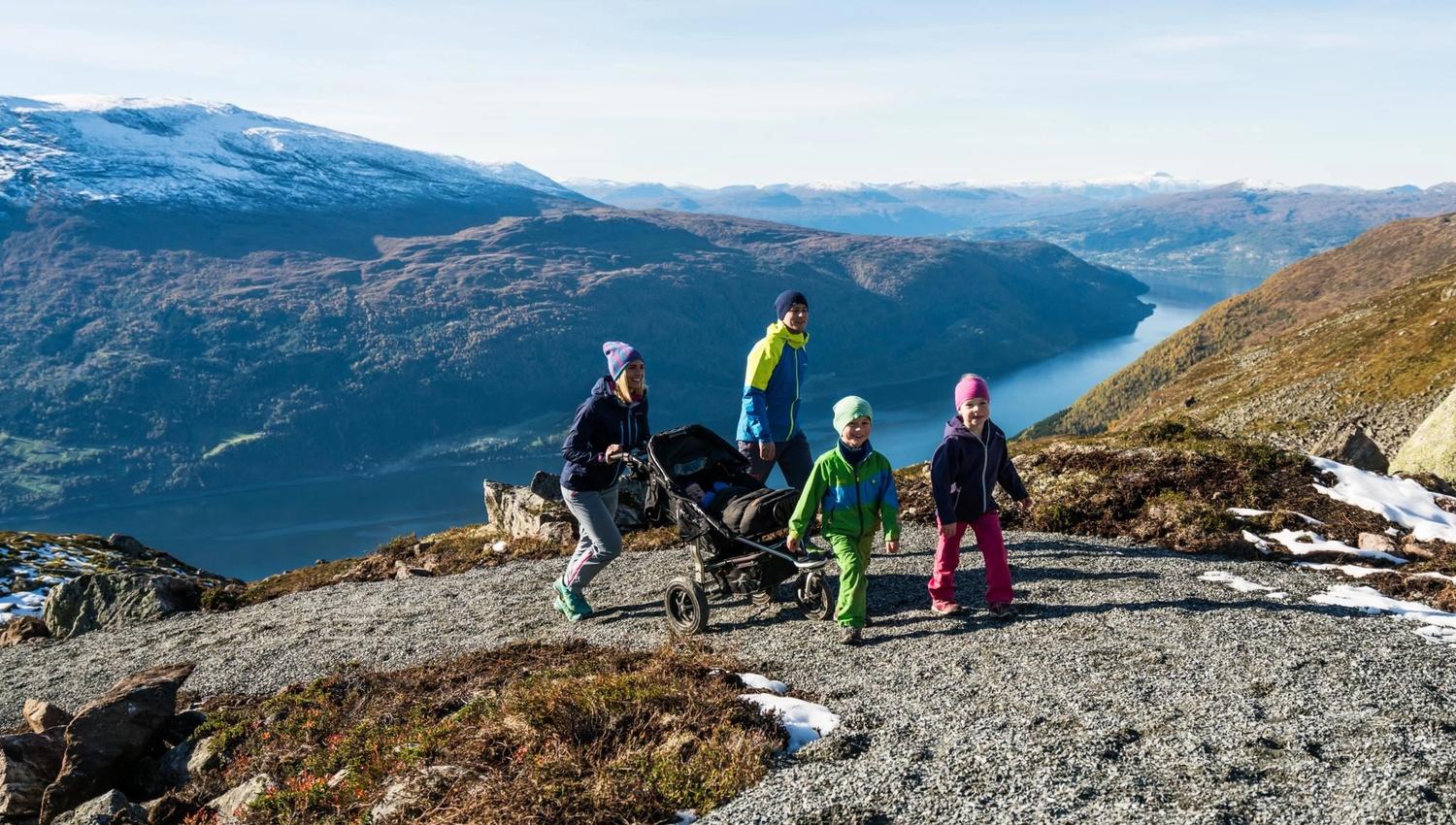 Hikers taking a break on the mountain at Hoven, with wide views of the surrounding fjord and mountains.