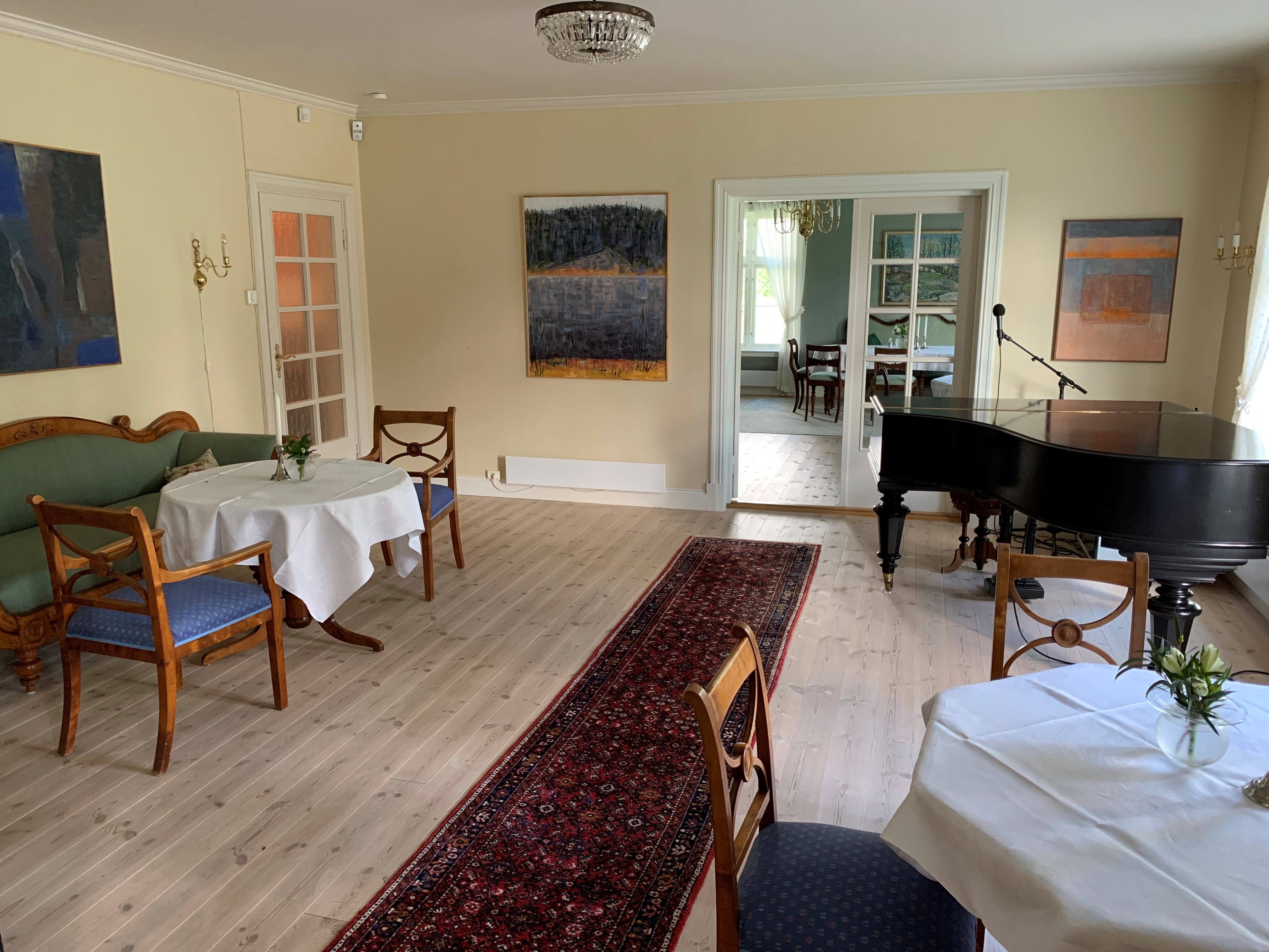 Et rom med to bord, stoler og et piano.