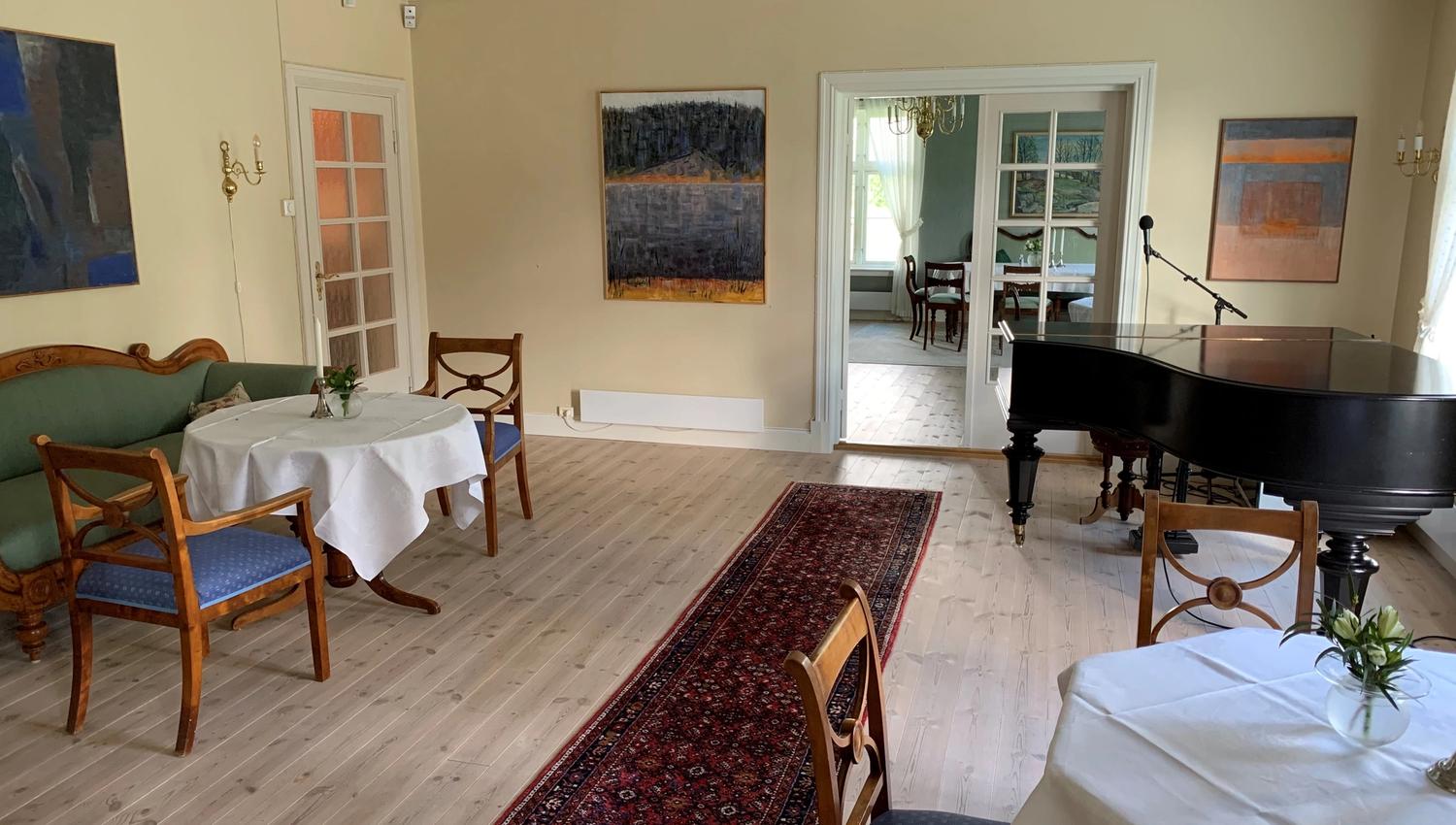 Et rom med to bord, stoler og et piano.
