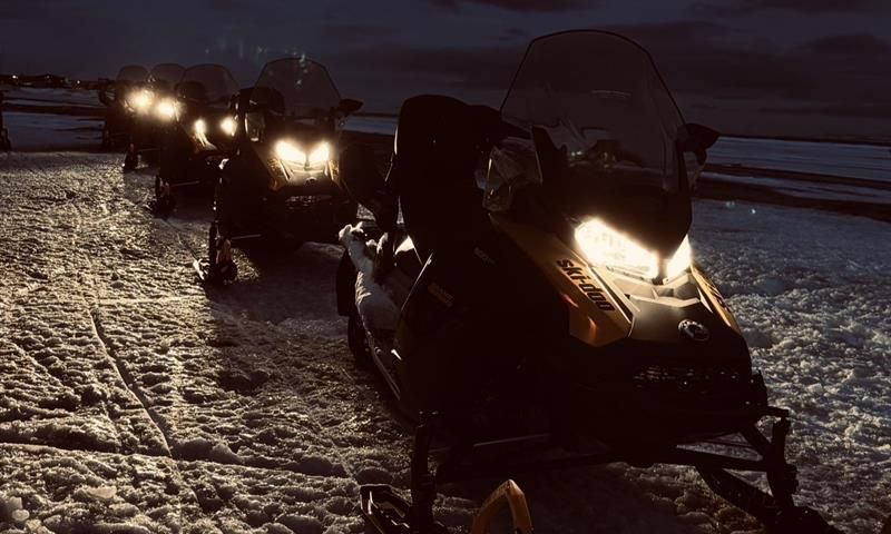 Snøscootere i mørket står parkert etterhverandre på linje.