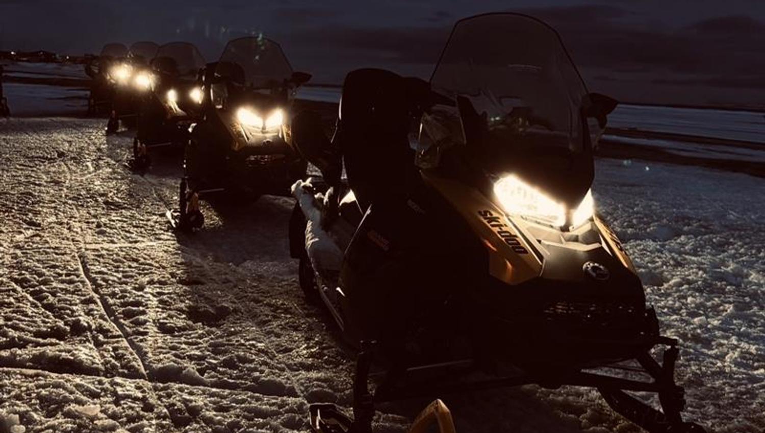 Snøscootere i mørket står parkert etterhverandre på linje.