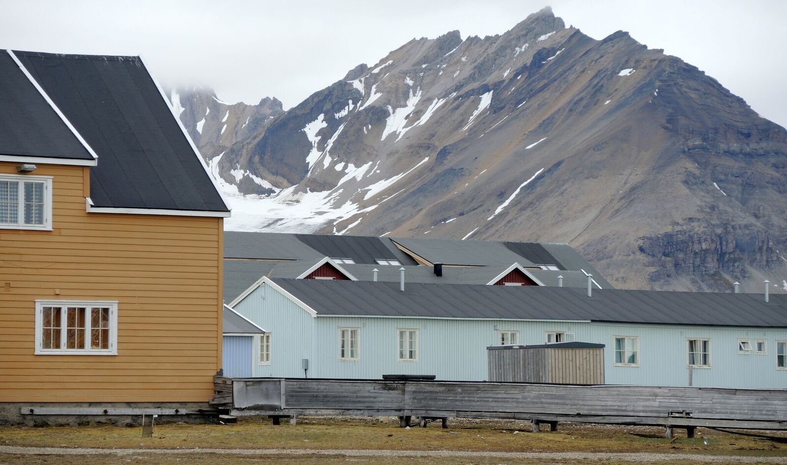 Buildings in Ny-Ålesund in the foreground, with a tall mountain in the background with small spots of snow