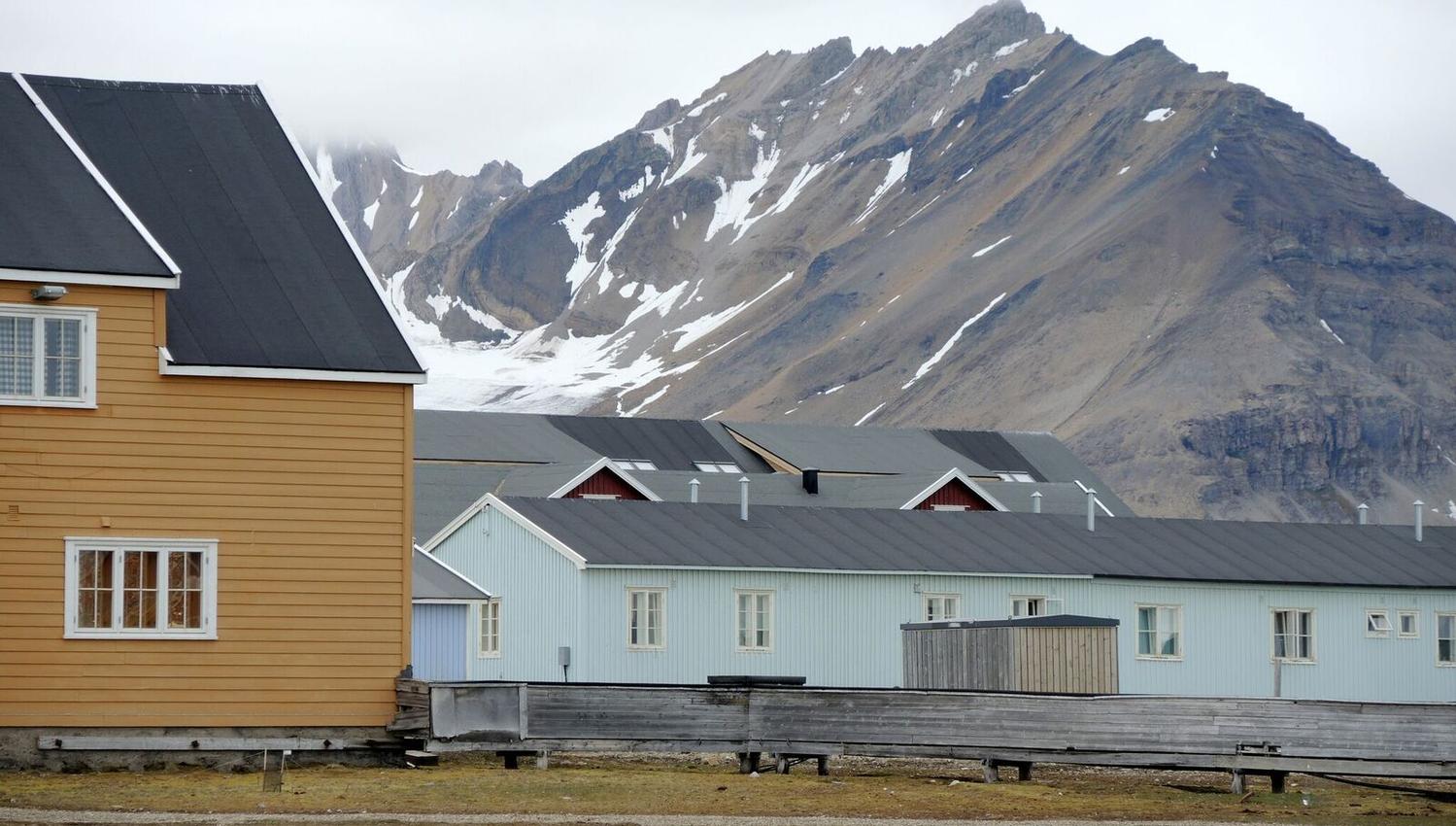 Buildings in Ny-Ålesund in the foreground, with a tall mountain in the background with small spots of snow