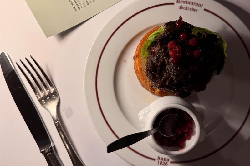 Open sandwich with tender meat and lingonberries served at Restaurant Schrøder, with the menu in the background.