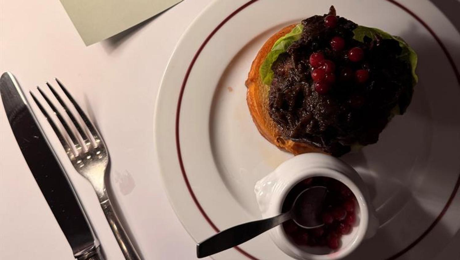 Open sandwich with tender meat and lingonberries served at Restaurant Schrøder, with the menu in the background.