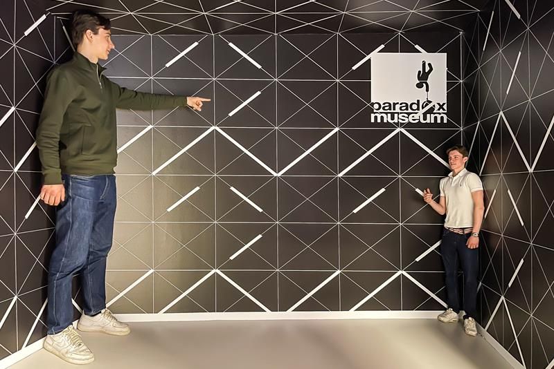 Black room with two boys appearing in different perspectives; one large the other small.