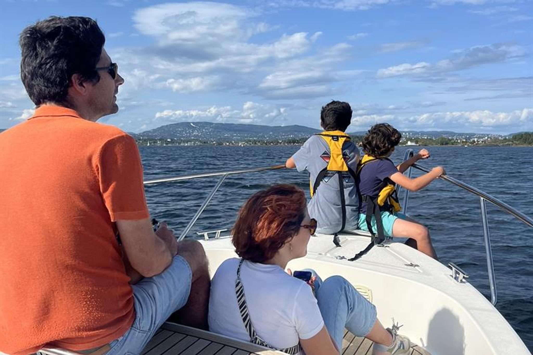 A family sits at the front of a boat enjoying a trip on the water in fine weather.