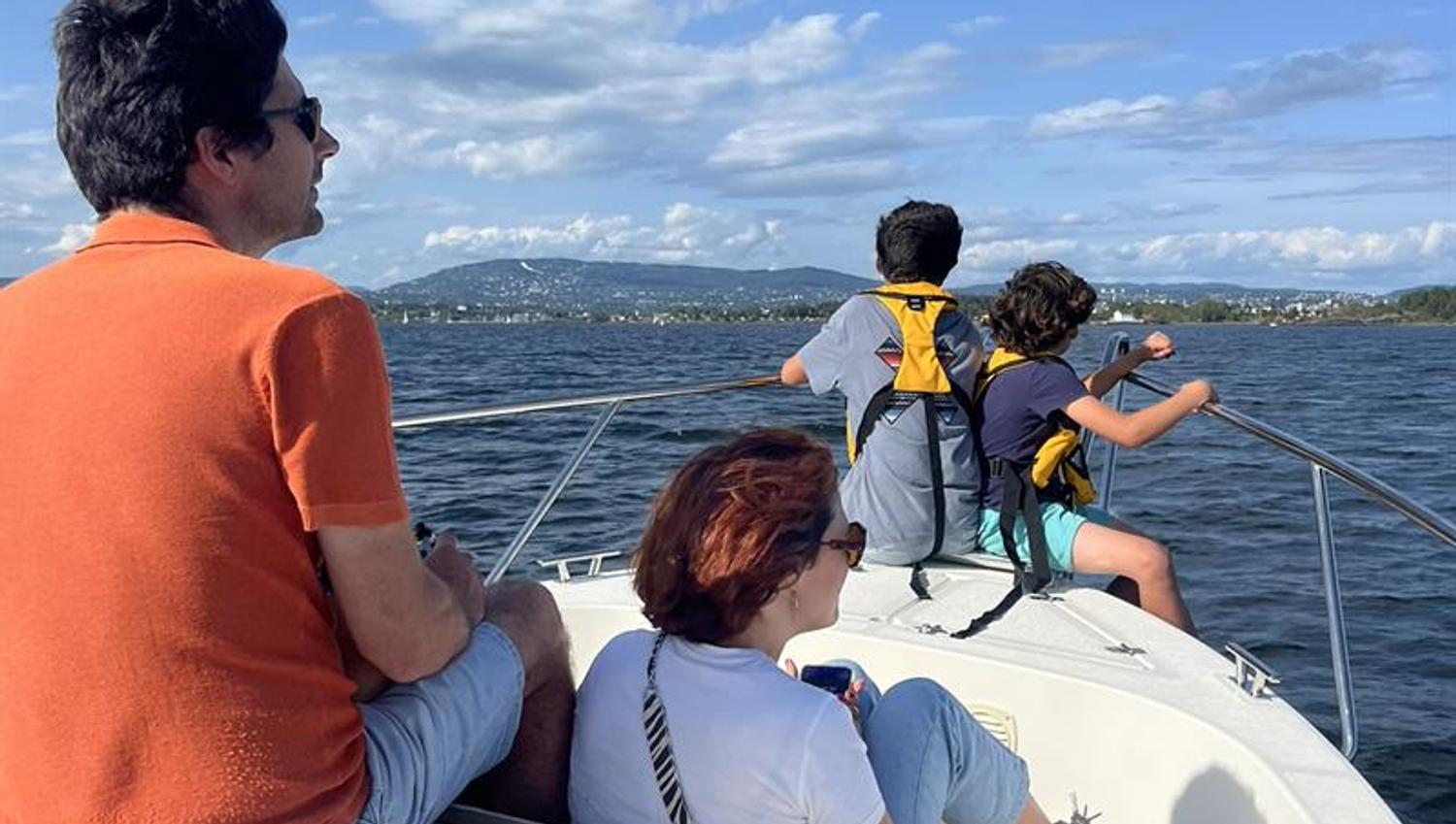 A family sits at the front of a boat enjoying a trip on the water in fine weather.