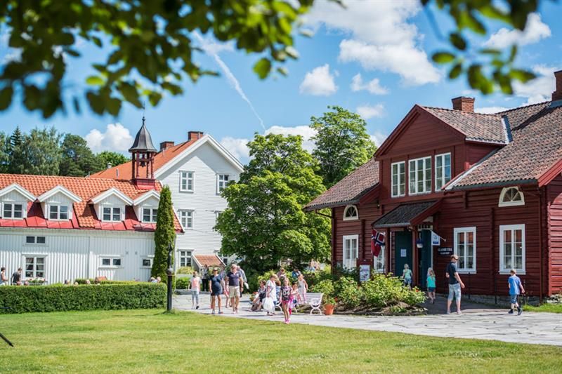 Solskinnsdag med trehus, gressplen og menensker som går.