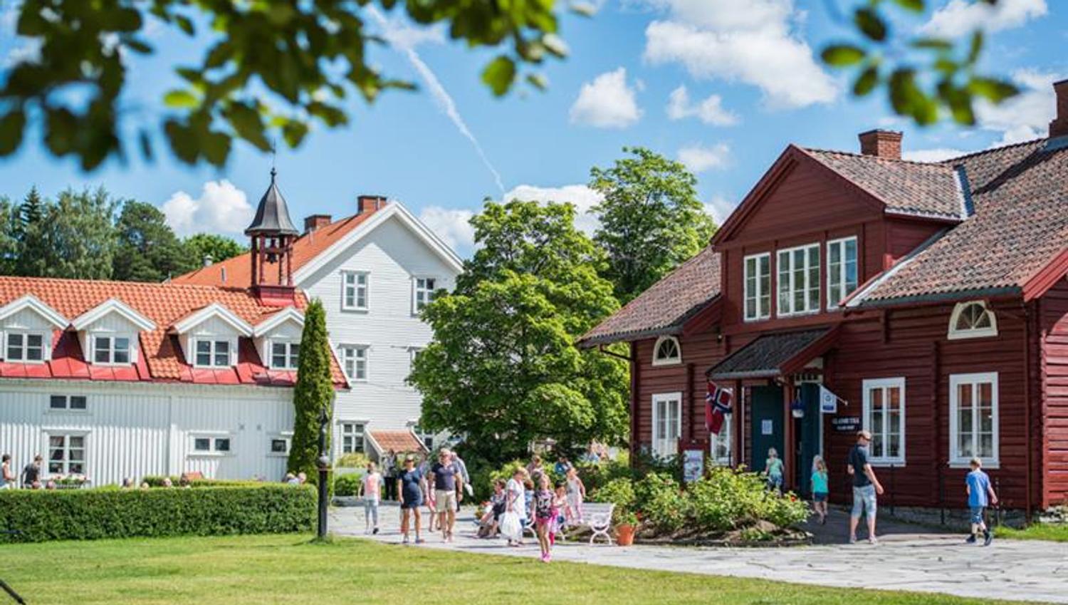 Solskinnsdag med trehus, gressplen og menensker som går.