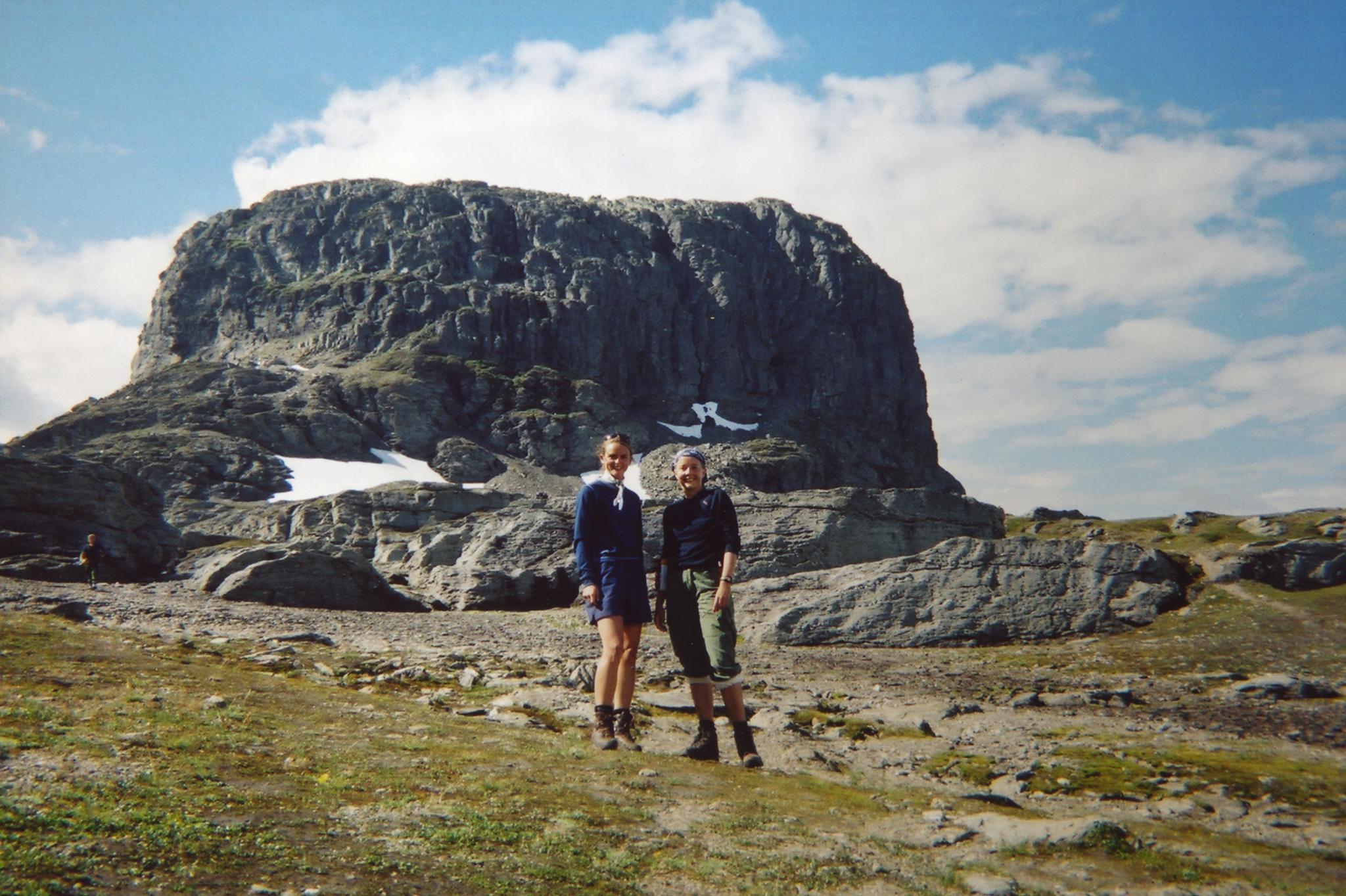 Two hikers on the Hardangervidda plateau with a dramatic mountain formation in the background on a clear summer day.