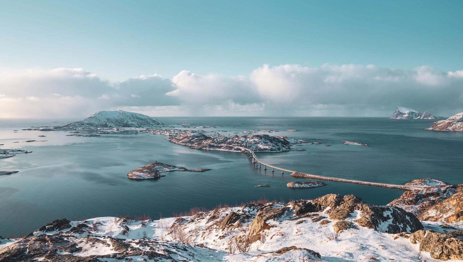 Snowy coastal landscape with bridges between islands and a clear sky in the background