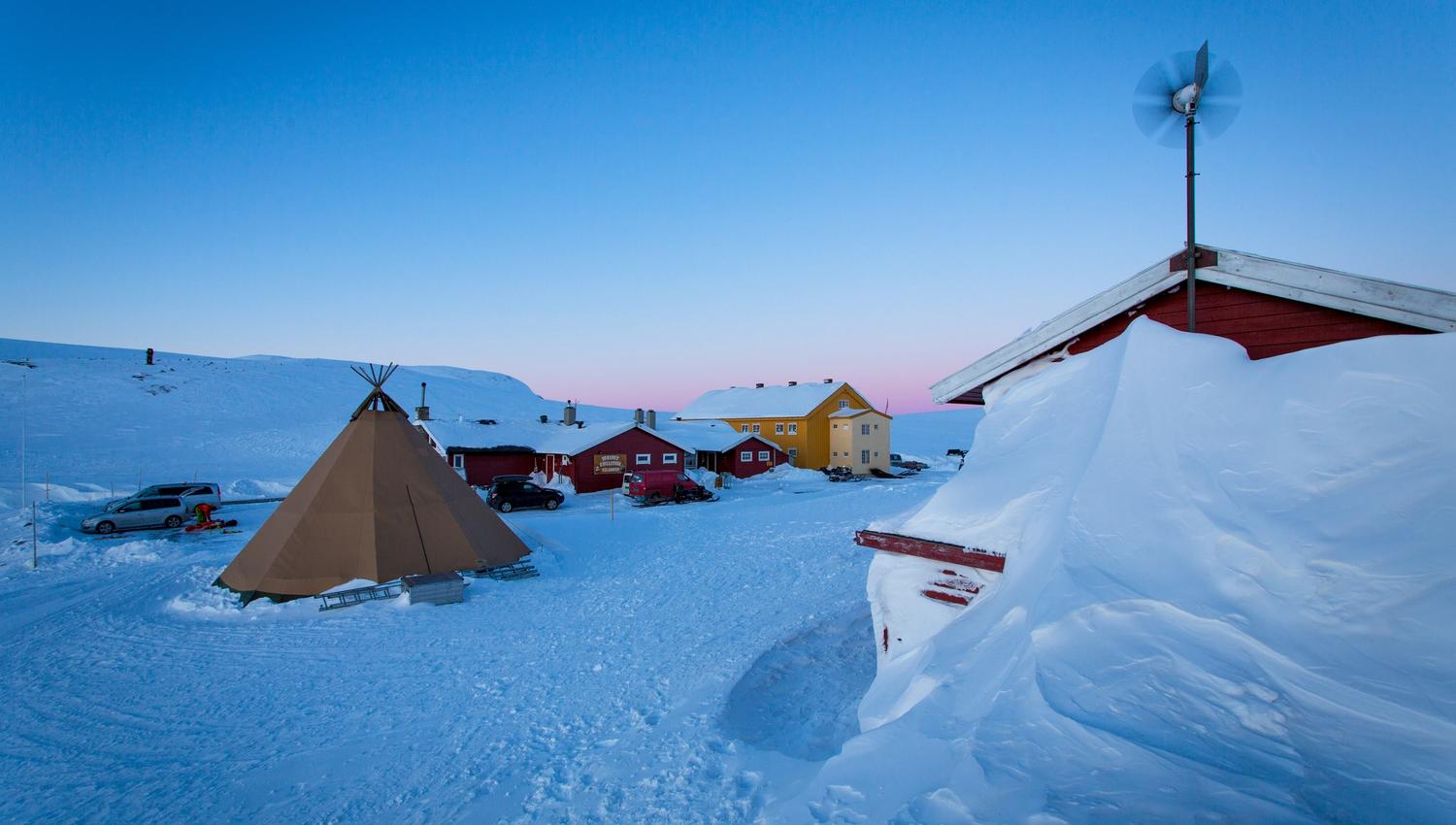 The red Dyranut Fjellstova and yellow Dyranut Turisthytta mountain lodges in snowy landscape.