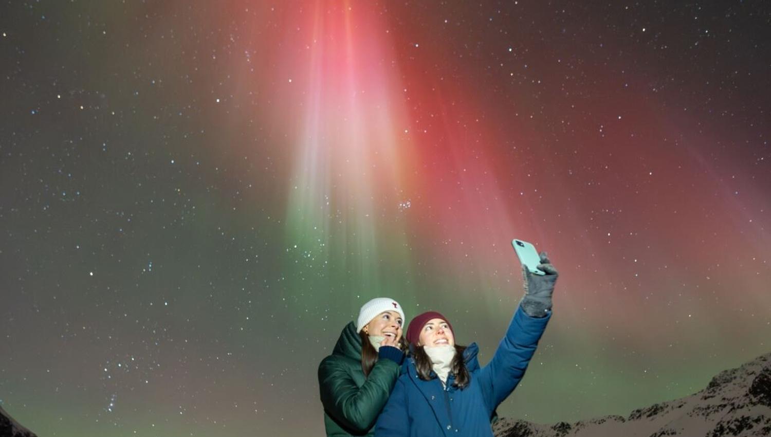 A couple takes a selfie with red Aurora in the background