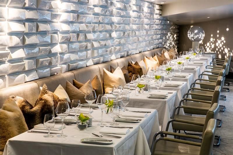 White, clothed tables, beige seating section, beige chairs, white textured walls and a beige ceiling.