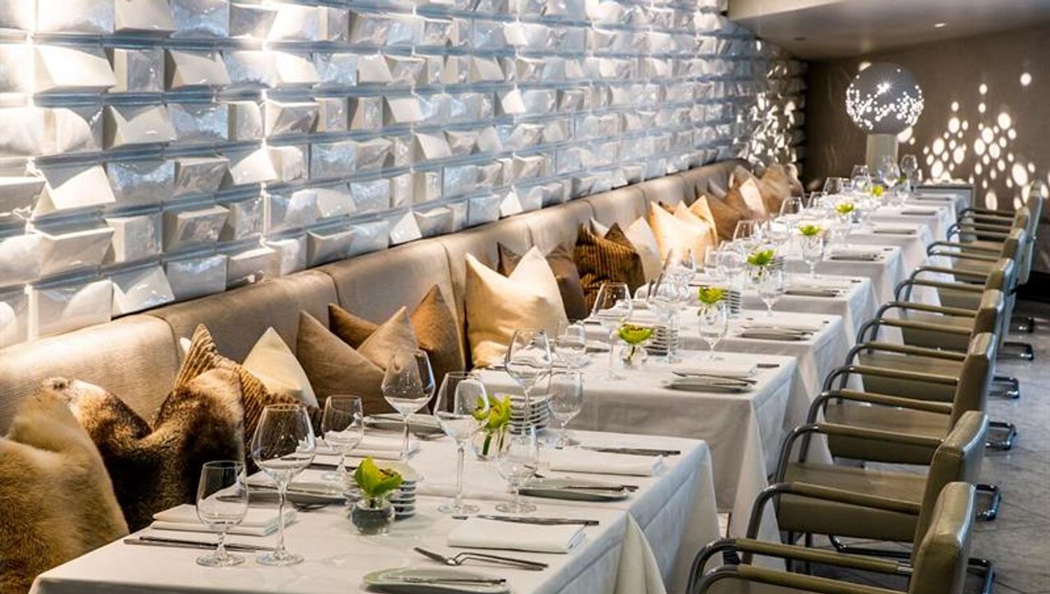 White, clothed tables, beige seating section, beige chairs, white textured walls and a beige ceiling.