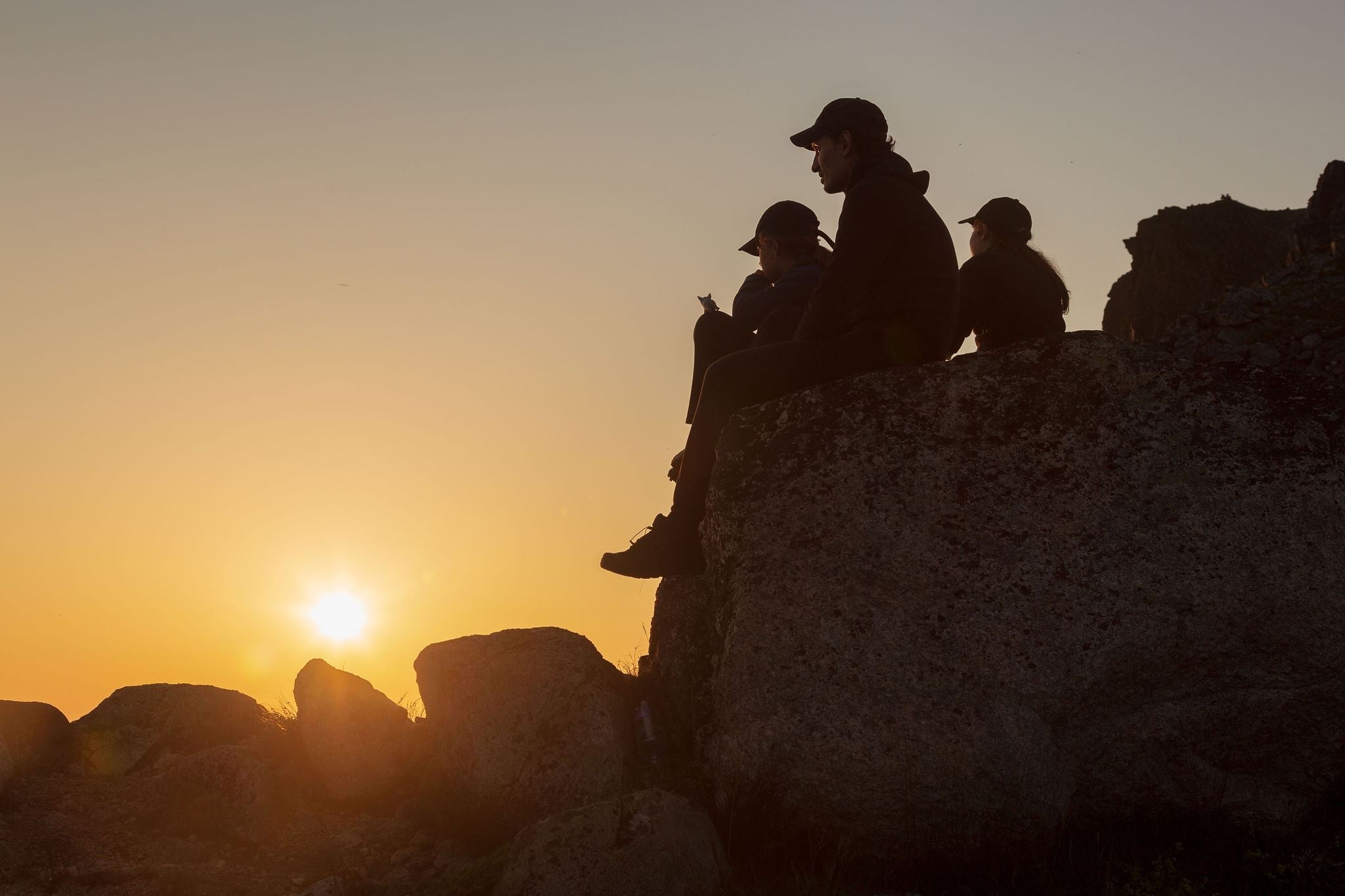 A group sitting on a rock and watching the midnight sun
