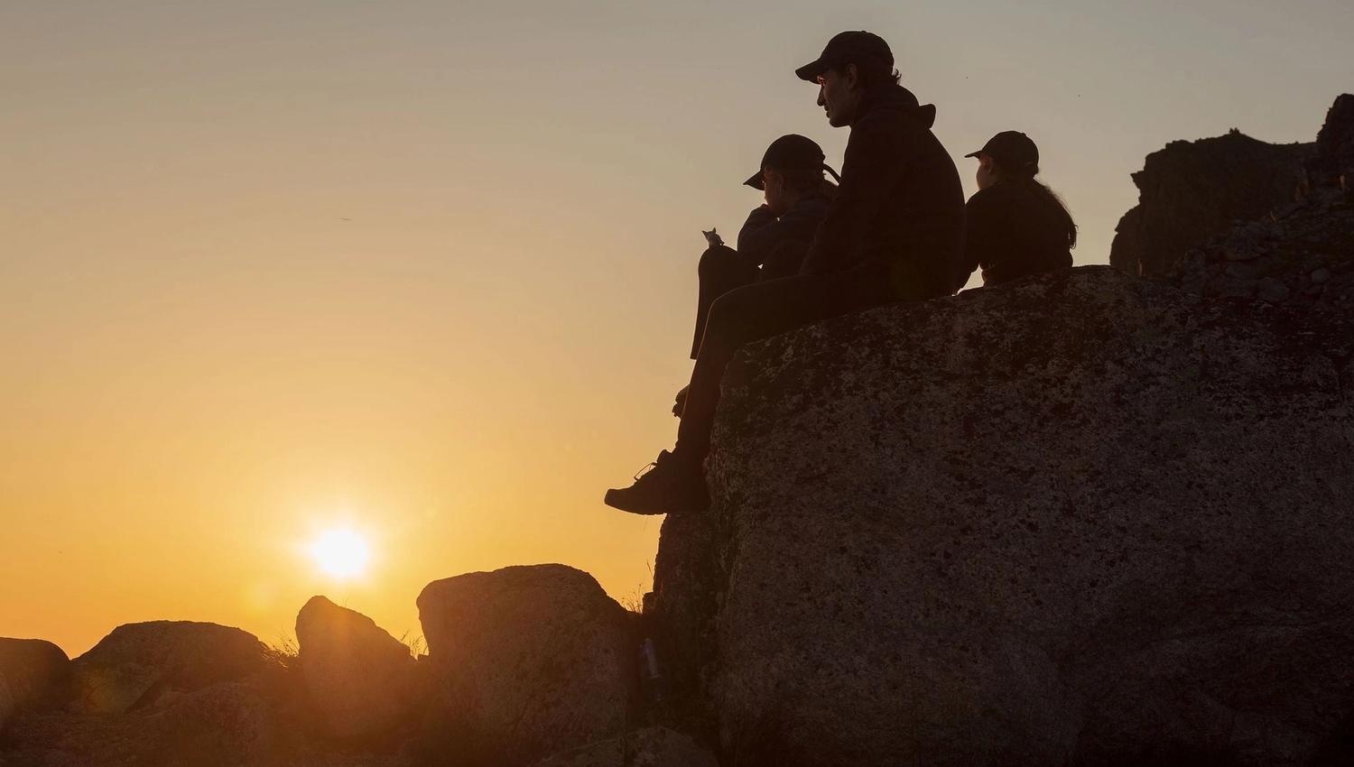 A group sitting on a rock and watching the midnight sun