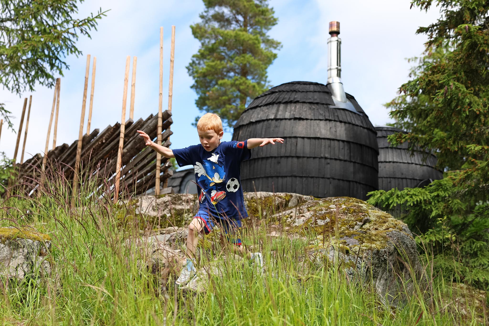 Barn som leker i gresset ved en tønneformet grillhytte i skogsomgivelser.