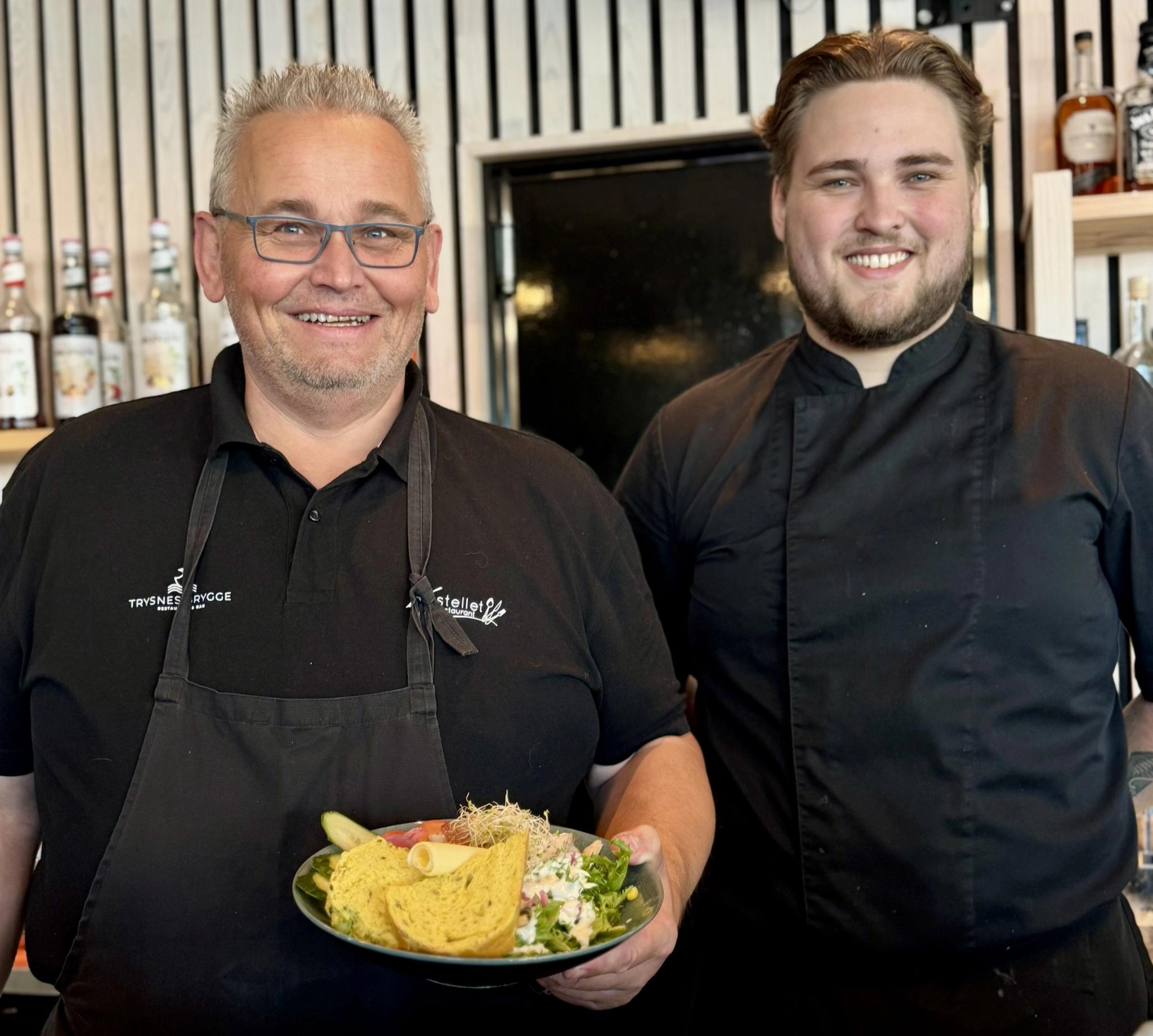 Two smiling chefs proudly showing a chicken salad.