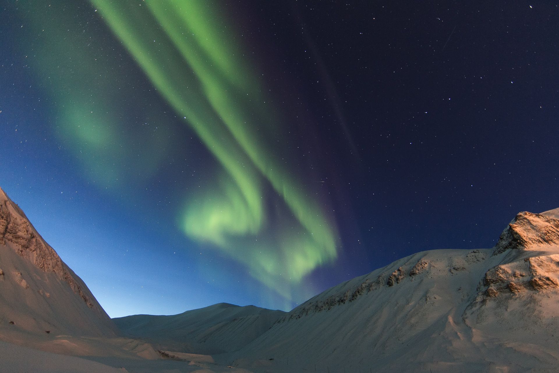 A mountainous landscape in the foreground with northern lights in the skies in the background